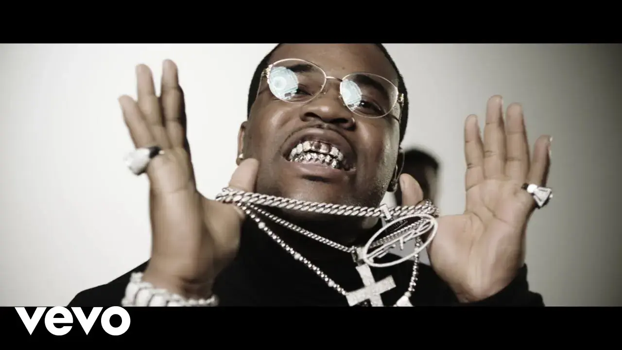 A$AP Ferg wears round sunglasses and holds up his hands and necklaces, with a Vevo logo below