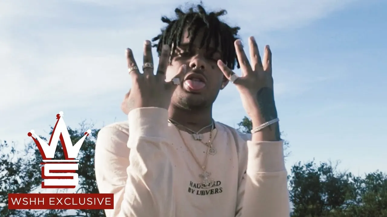 Smokepurpp raises both hands outside under a blue sky, with the WSHH logo in the corner